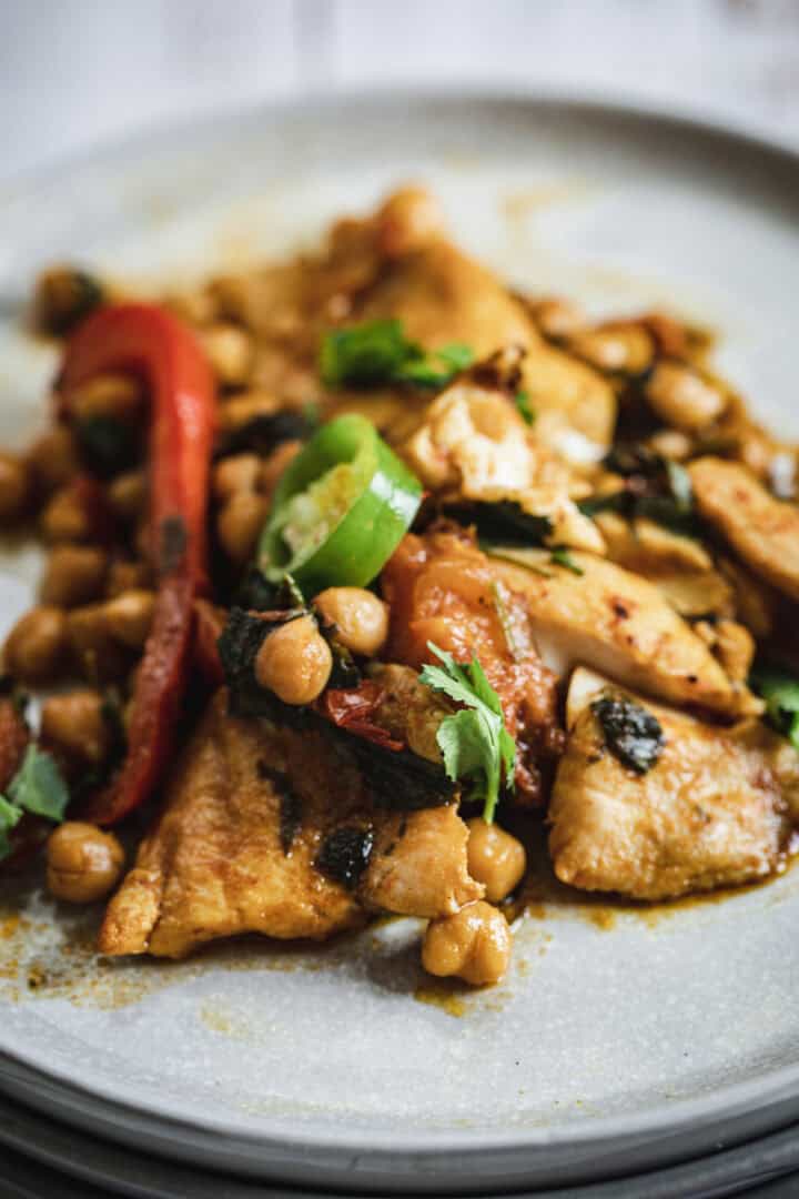 Grilled chicken with chickpeas, red peppers, herbs, and sliced green chili on a gray plate.