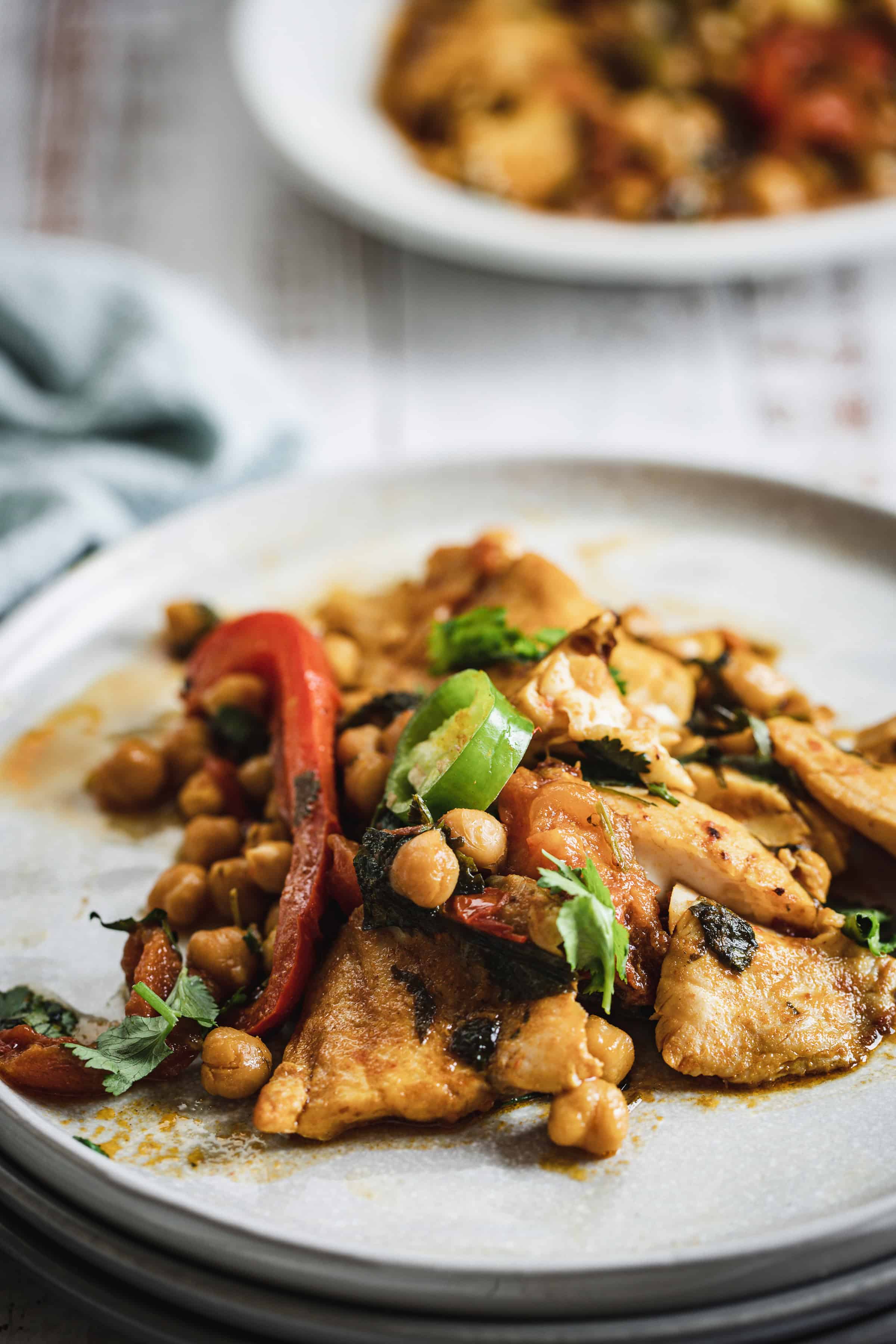 A plate of cooked chickpeas, vegetables, and tofu garnished with fresh herbs on a light grey plate.