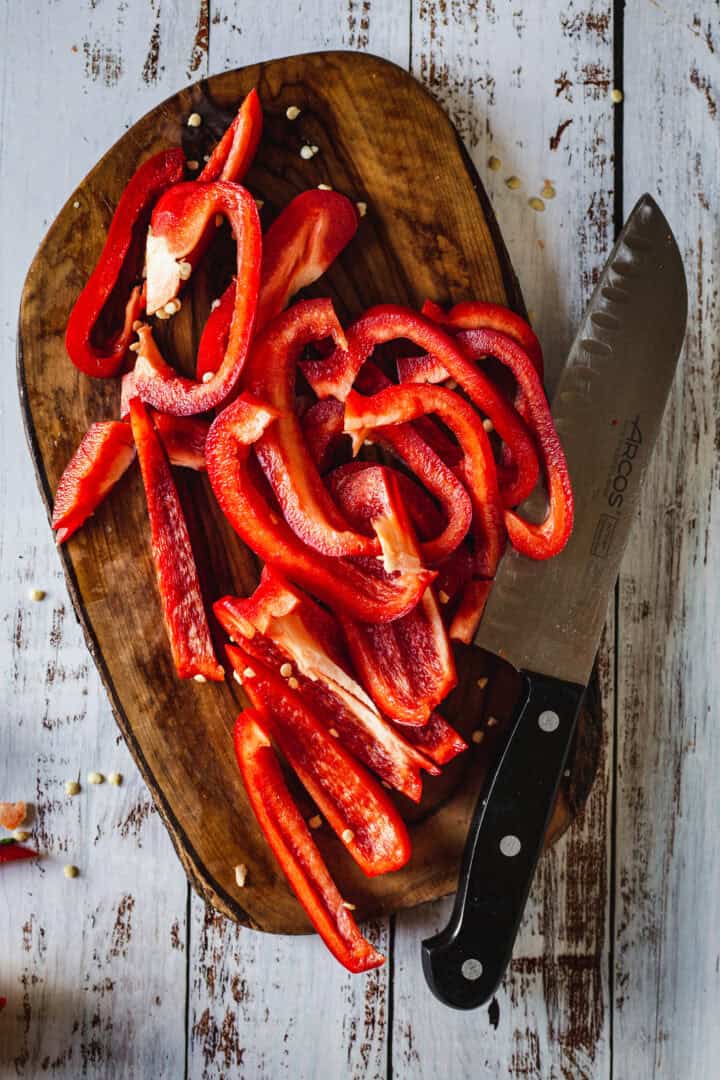 Sliced red bell pepper and a chef's knife on a wooden cutting board.