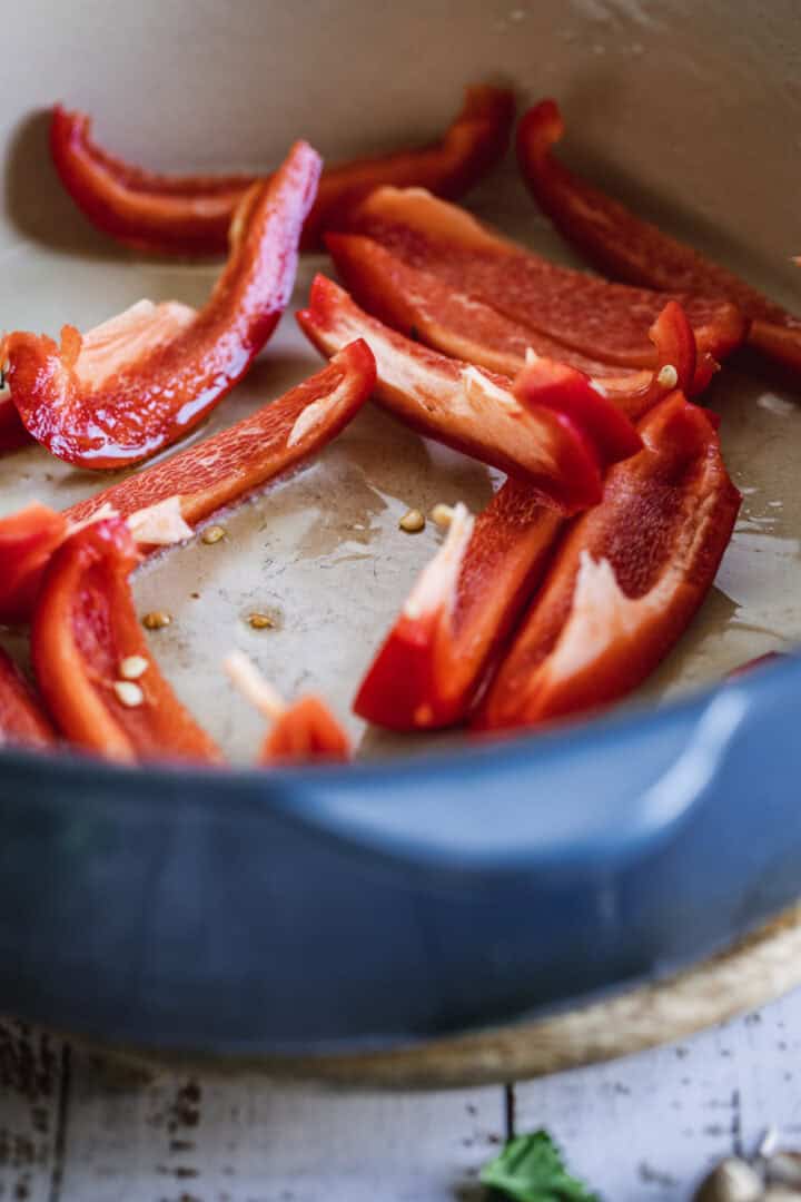 Sliced red bell peppers in a blue pot, ready for cooking.