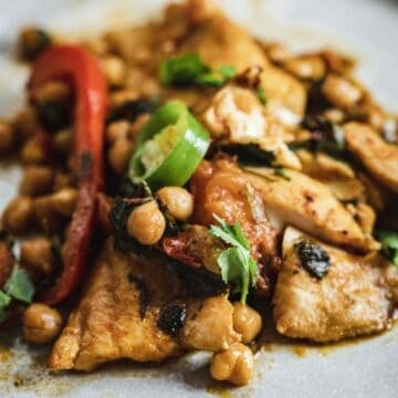 Close-up of a spicy chickpea and chicken dish with sliced peppers and fresh cilantro on top.