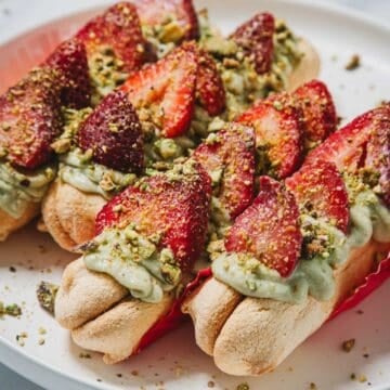 No-Bake Strawberry Pistachio Ladyfingers Dessert featuring ladyfingers topped with green pistachio cream, sliced strawberries, and crushed pistachios on a plate.
