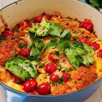 Baked egg dish in a blue pan with cherry tomatoes, avocado slices, and fresh cilantro on top.