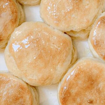 Golden brown biscuits with a shiny, glazed surface arranged closely together on a white background.