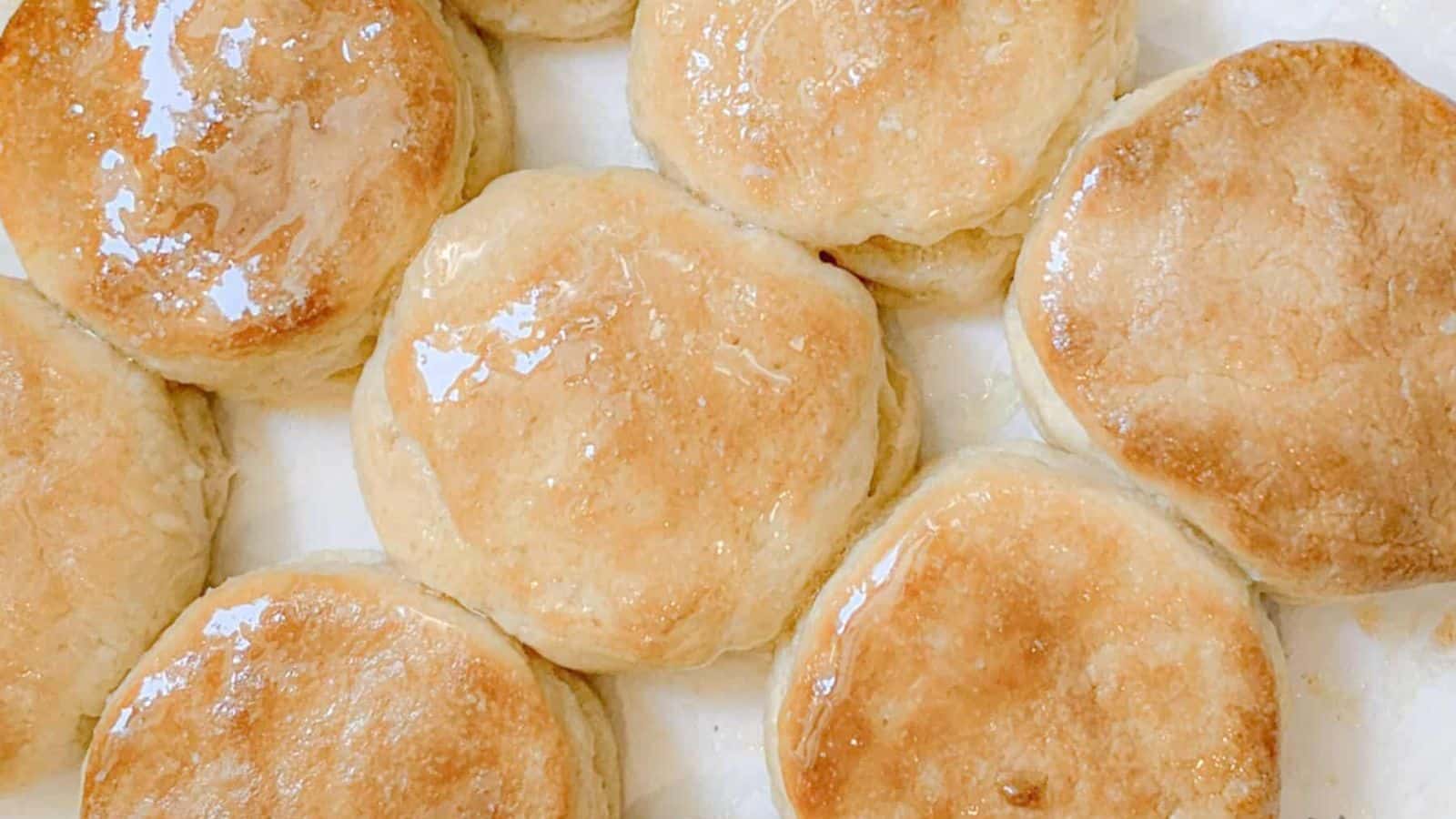 Golden brown biscuits with a shiny, glazed surface arranged closely together on a white background.