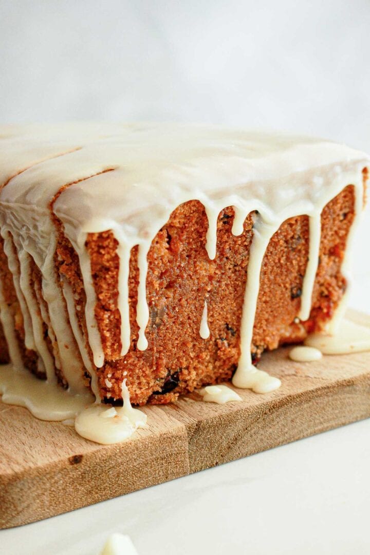 A loaf cake with white icing dripping down the sides, sitting on a wooden cutting board.