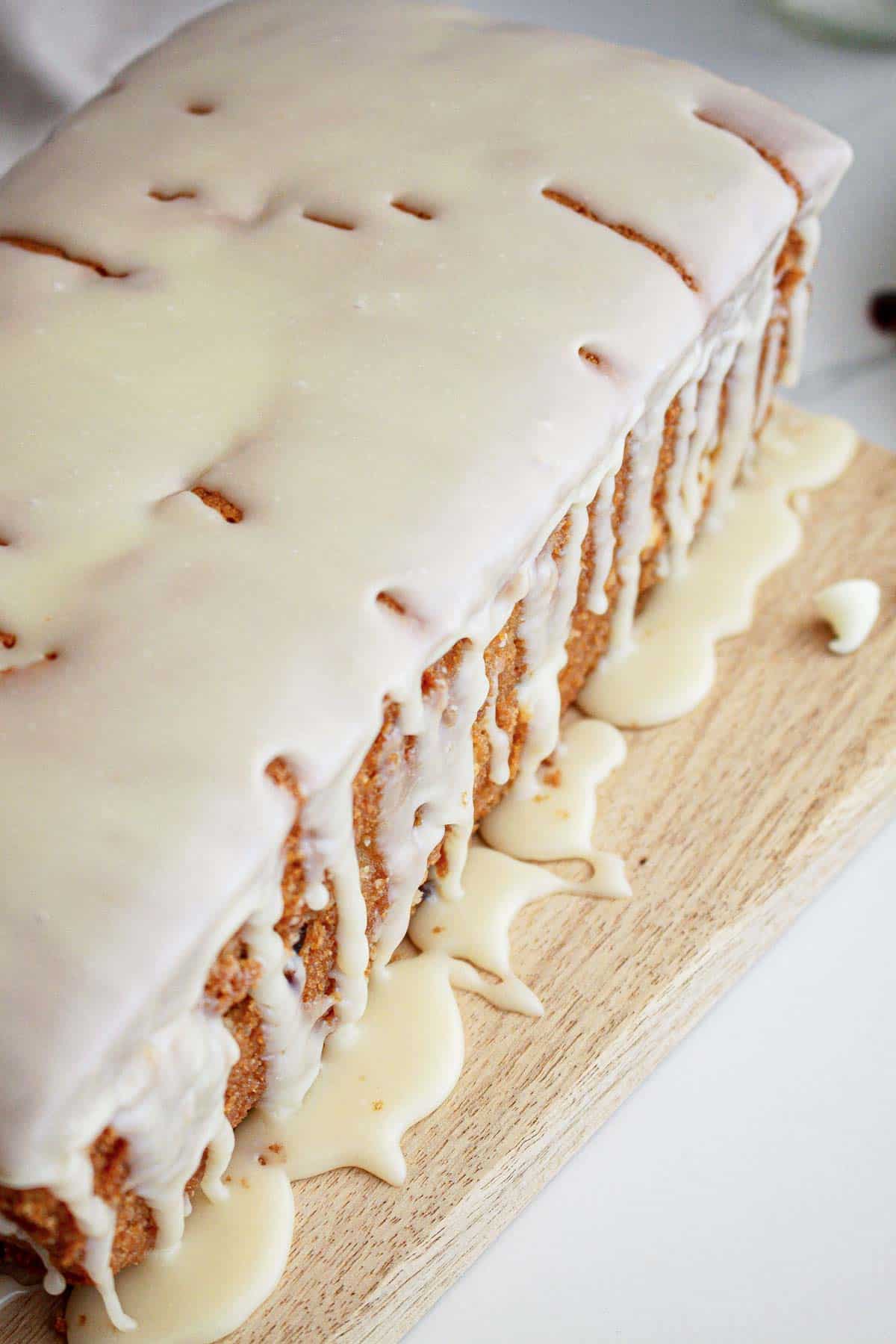 A loaf cake on a wooden board with white icing dripping down the sides and pooling at the base.