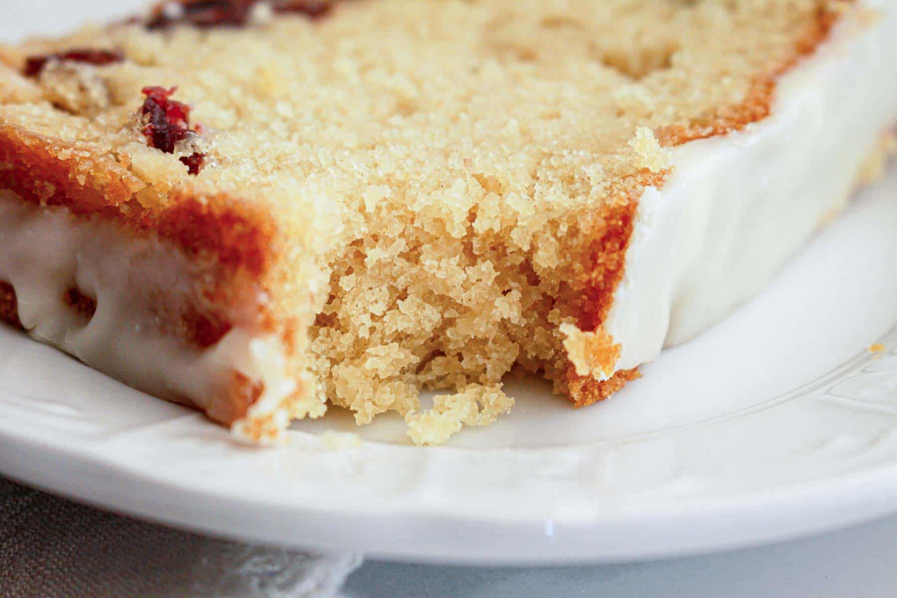 A close-up of a slice of moist cake with white icing on a white plate.