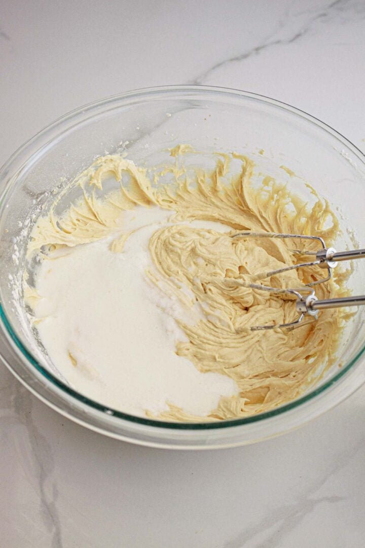 A glass bowl with cake batter and a hand mixer on a white countertop.