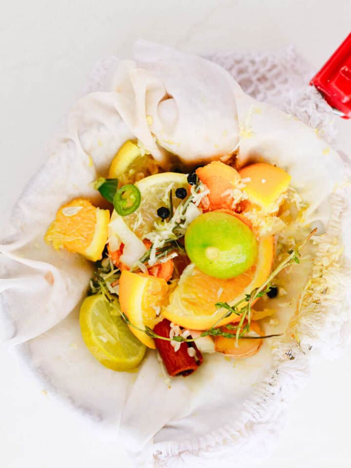 A cloth holds citrus fruit slices, herbs, and spices, ready for flavoring or making broth.