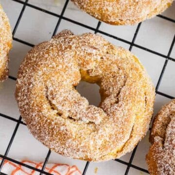 Close-up of sugar-coated cruller donuts cooling on a black wire rack.