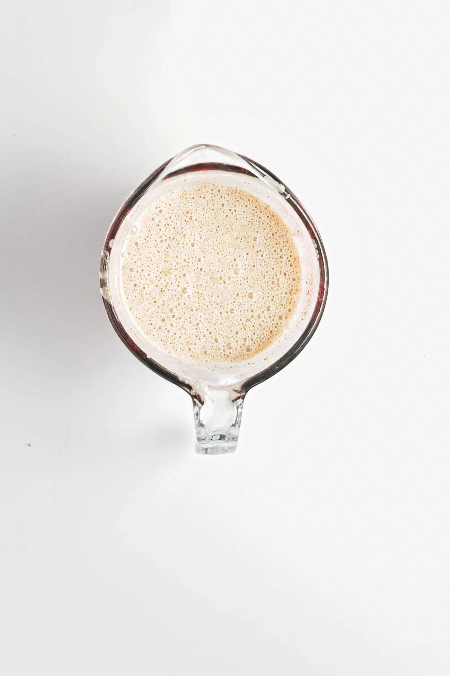 Top view of a glass measuring cup filled with a frothy beige liquid, the perfect base for Blueberry Coconut Almond Overnight Oats, on a white background.