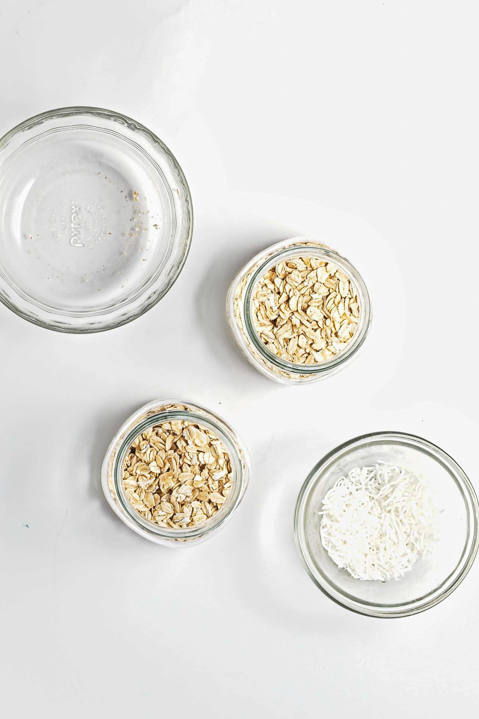 Three glass bowls on a white surface hold oats, shredded coconut, and an empty bowl-perfect for preparing Blueberry Coconut Almond Overnight Oats.