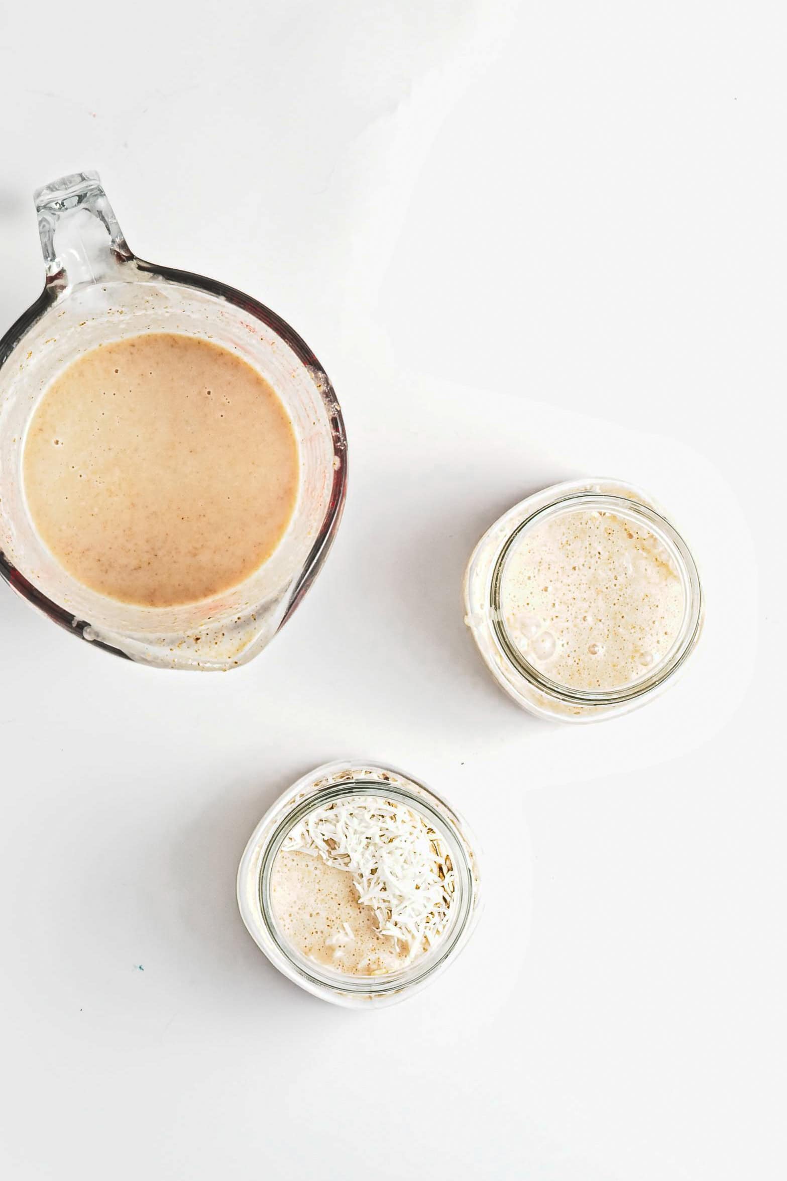 Two glass jars and a measuring cup with bubbly sourdough starter, perfect for pairing with Blueberry Coconut Almond Overnight Oats, on a white background.
