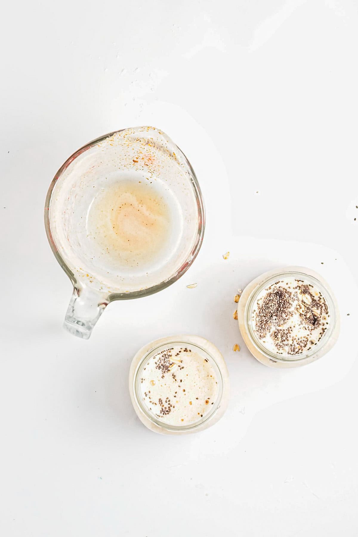 Top view of a glass measuring cup with residue and two small jars of Strawberry Almond Overnight Chia Oats, each creamy dessert sprinkled with cocoa.