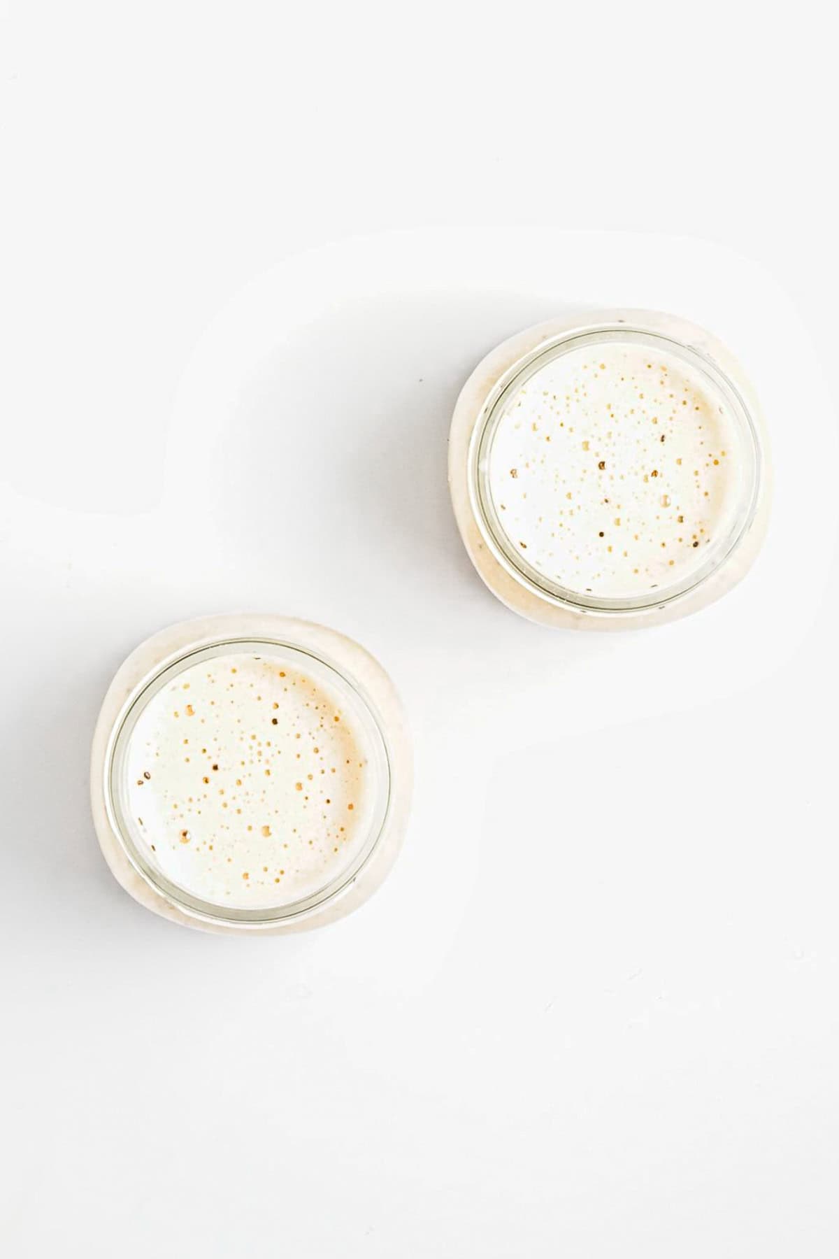 Two glass jars of sourdough starter seen from above, with bubbles on the surface, on a white background-perfect alongside a wholesome breakfast like Strawberry Almond Overnight Chia Oats.