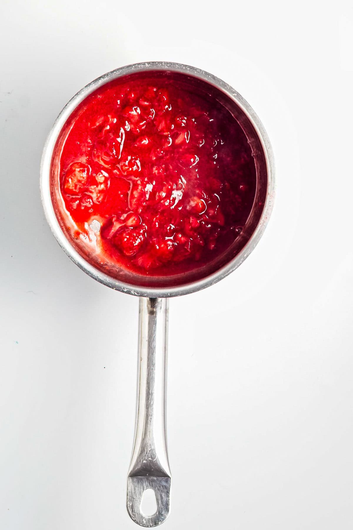 A saucepan filled with bright red strawberry sauce, perfect for topping your Strawberry Almond Overnight Chia Oats, sits on a white background.