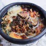 Baked cheese dish topped with herbs, nuts, and figs in a rustic black bowl.