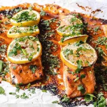 Baked salmon fillets topped with lemon slices and fresh herbs on a sheet of parchment paper—a classic addition to your collection of Salmon Dishes.