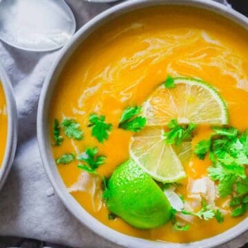 A bowl of creamy orange soup garnished with lime slices, herbs, and shredded chicken.