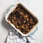 A baking dish filled with crispy, browned gluten free stuffing sits on a checkered kitchen towel on a marble surface.