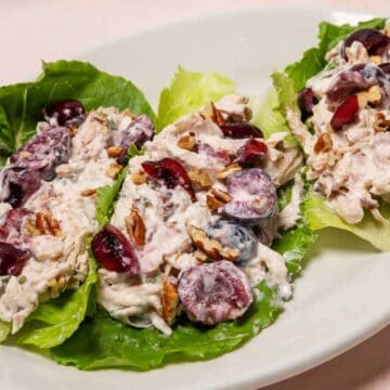 Three lettuce leaves topped with chicken salad, grapes, and pecans on a white oval plate.
