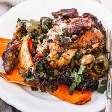 Roast chicken with olives and capers served on roasted sweet potato wedges, garnished with fresh herbs.