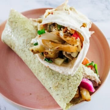 A pita wrap filled with grilled vegetables and herbs on a pink plate.
