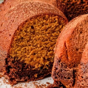 A close-up of a sliced Bundt cake dusted with cocoa powder on a white plate.