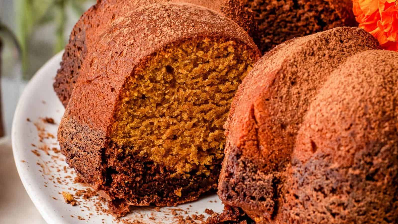 A close-up of a sliced Bundt cake dusted with cocoa powder on a white plate.