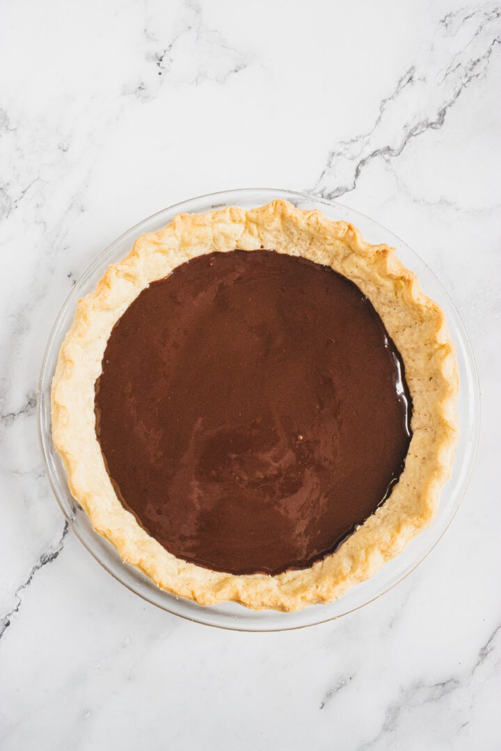 Chocolate pie with a baked crust on a white marble surface, viewed from above.