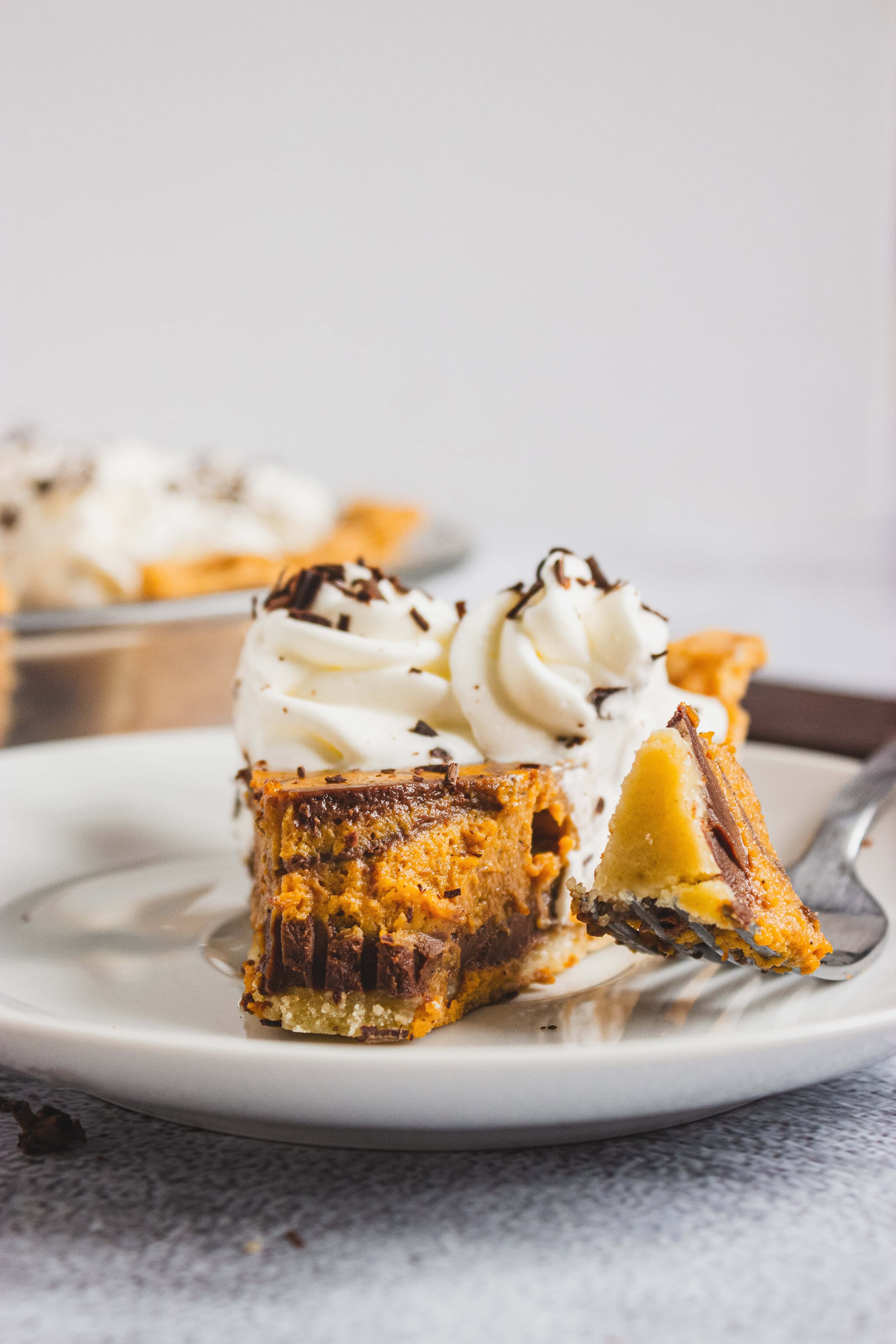 A close-up of a fork holding a slice of creamy pie topped with whipped cream and chocolate shavings.