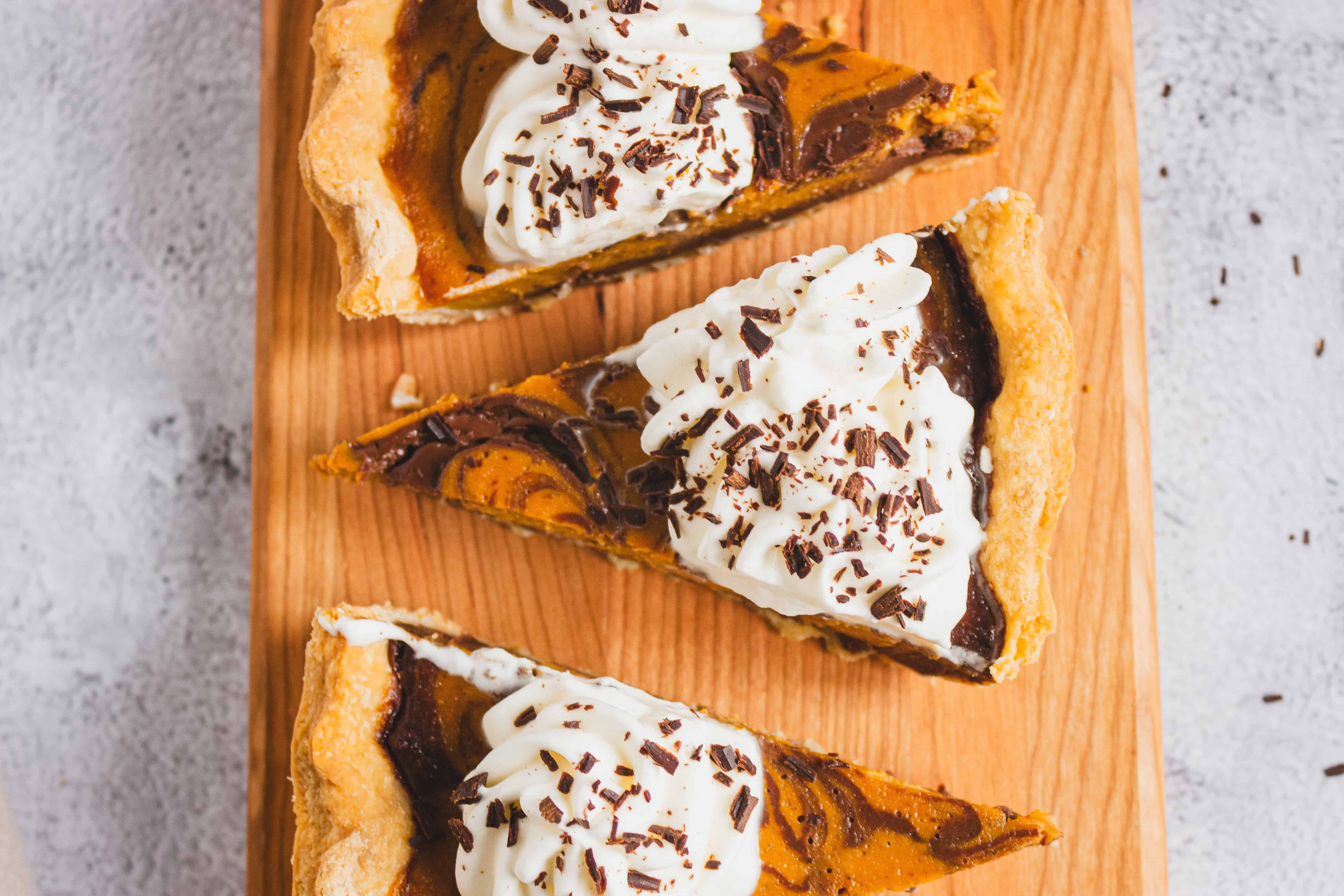 Three slices of pie topped with whipped cream and chocolate shavings on a wooden board.