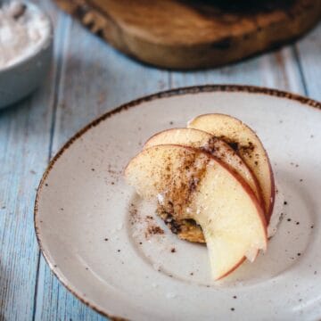 Sliced apple with cinnamon on a small plate, with dip and crackers on a rustic wooden table.