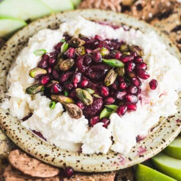 Ricotta cheese dip topped with pomegranate seeds, pistachios, and green onions, served with crackers and apples.