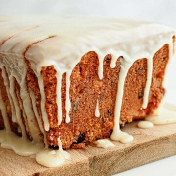 A loaf cake with white icing dripping down the sides, placed on a wooden board.