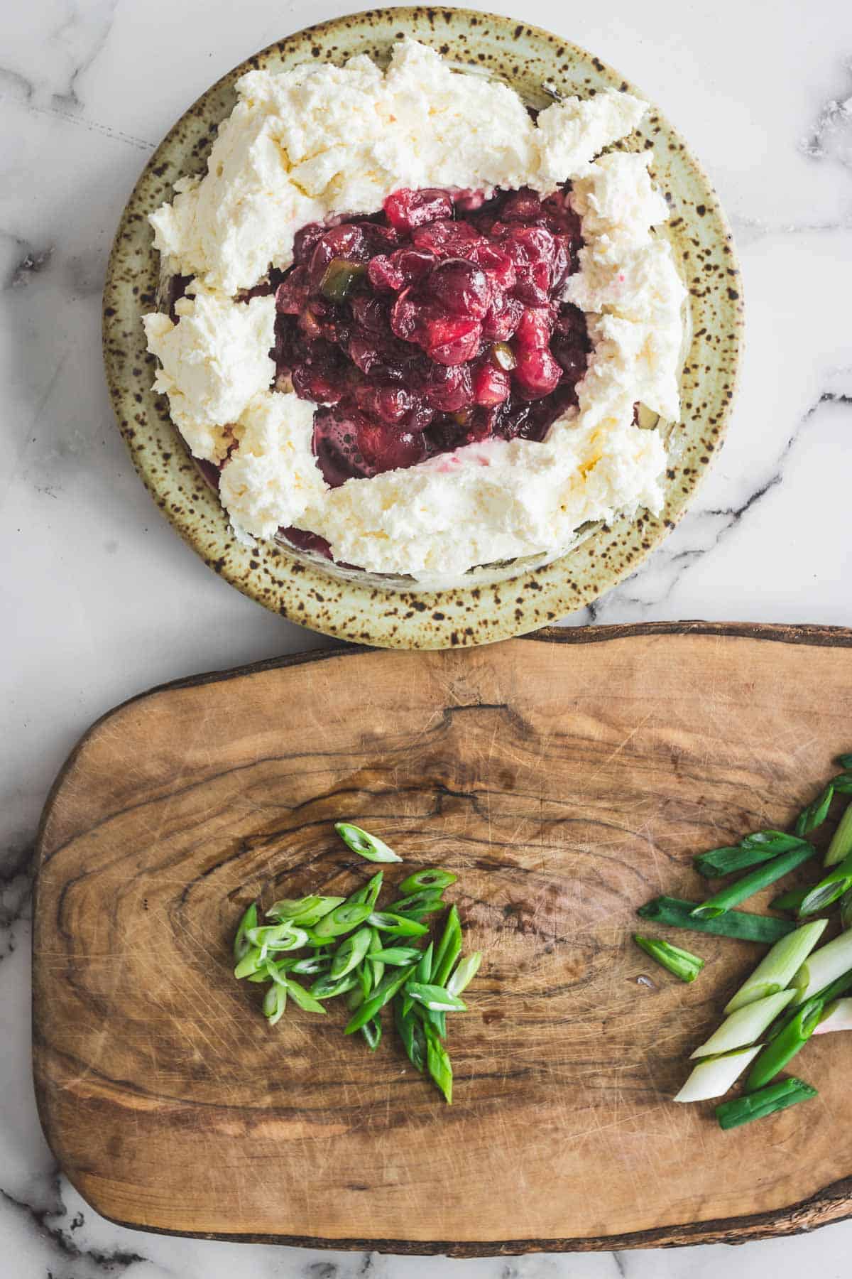 A plate with whipped cheese and cranberry dip, alongside a cutting board topped with sliced green onions.
