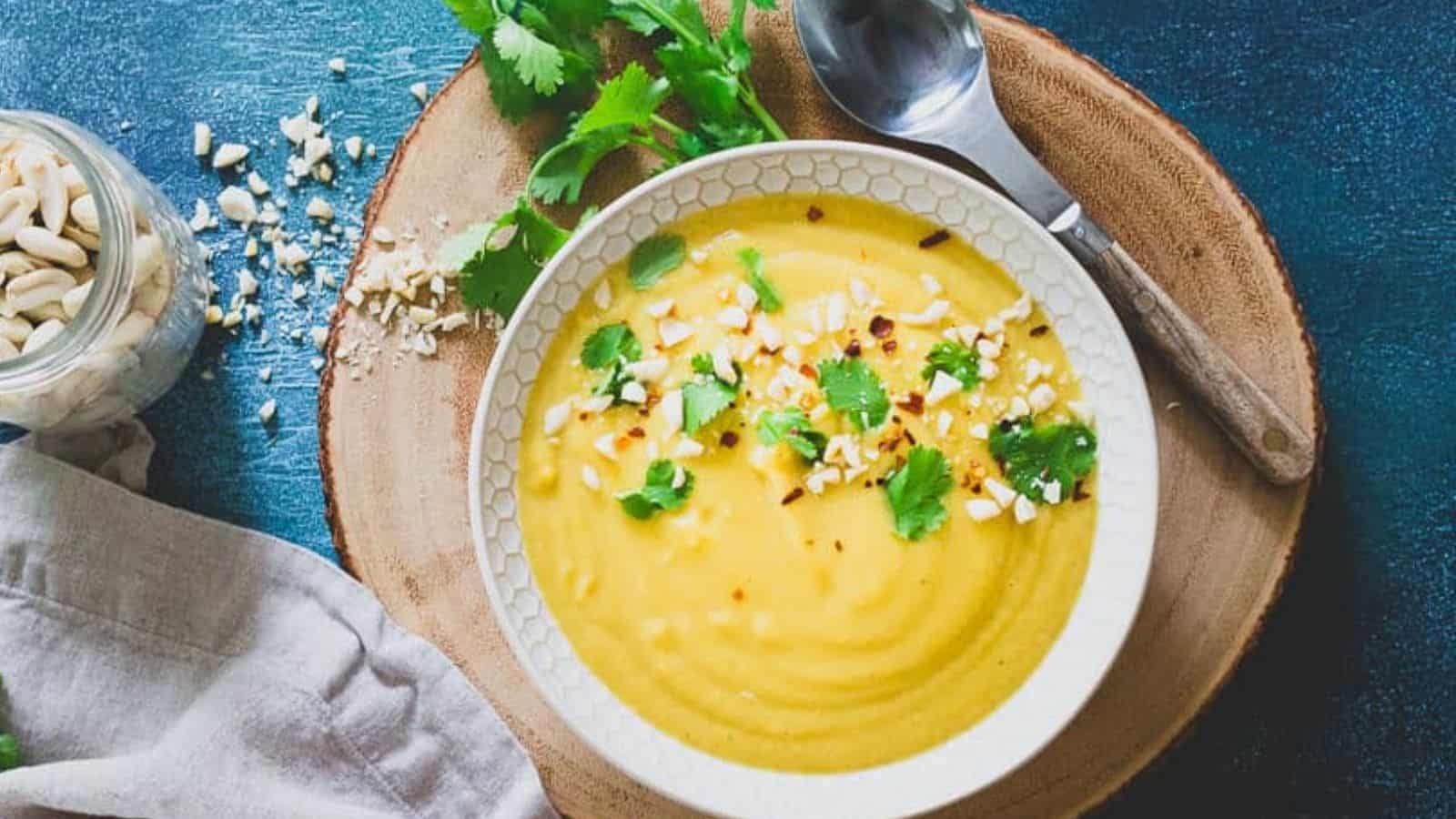 A bowl of delicata squash soup with a spoon on a wooden table.