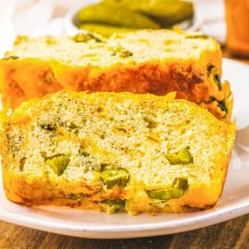 Two slices of savory bread with visible pieces of pickles on a white plate, served on a wooden board.