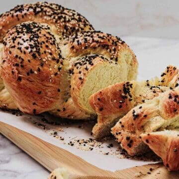 A braided loaf of seeded bread, partially sliced, on a wooden board.
