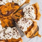Slice of marbled pumpkin pie with whipped cream and chocolate shavings on a pie server.