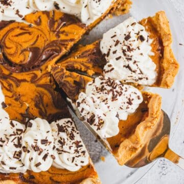 Slice of marbled pumpkin pie with whipped cream and chocolate shavings on a pie server.