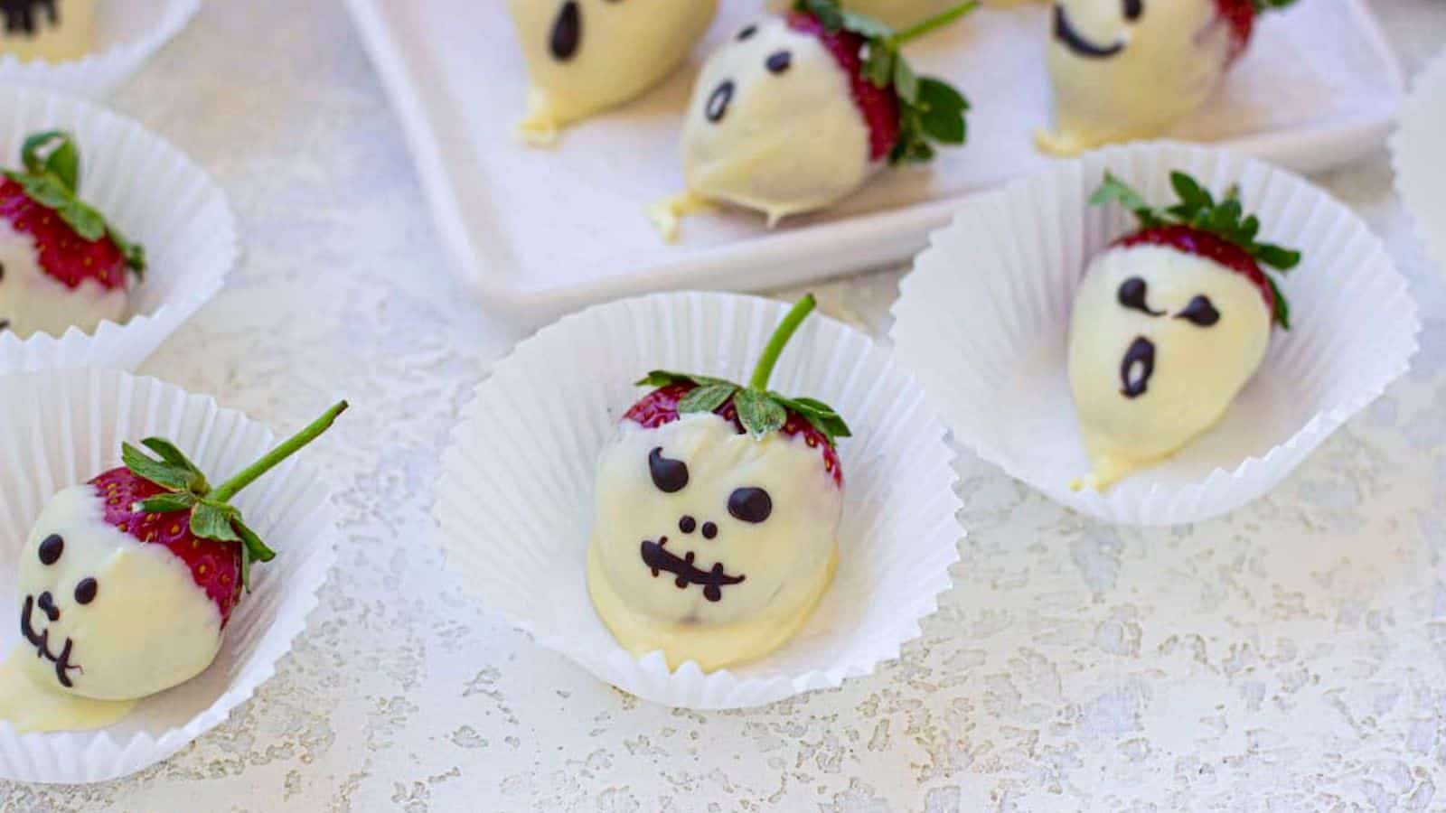 Several chocolate covered strawberries decorated as Halloween ghosts on the table.
