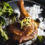 Roasted duck leg on white rice, topped with sliced green onions, served with broccoli.