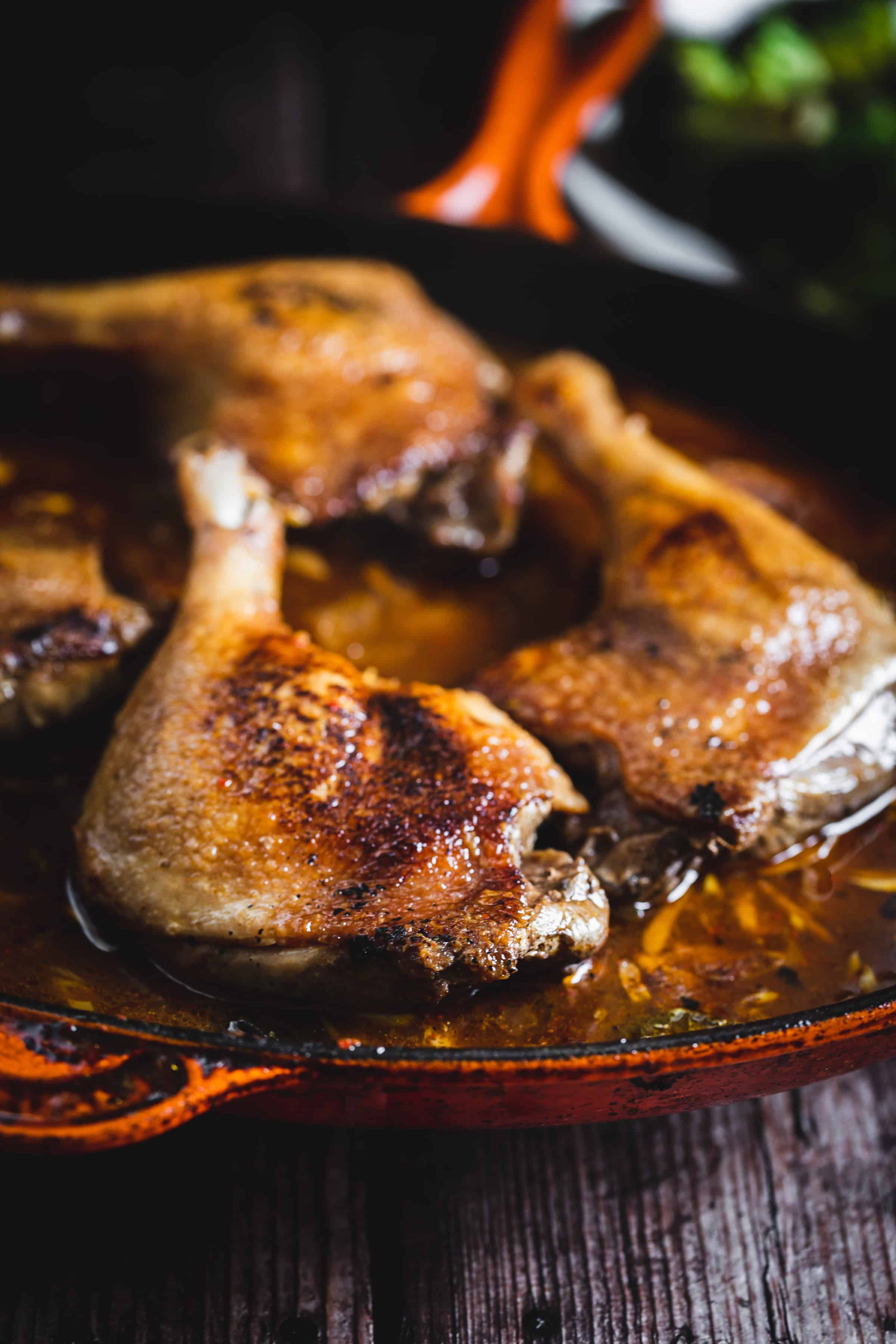 Golden-brown roasted chicken legs cooking in a cast iron skillet with sauce.