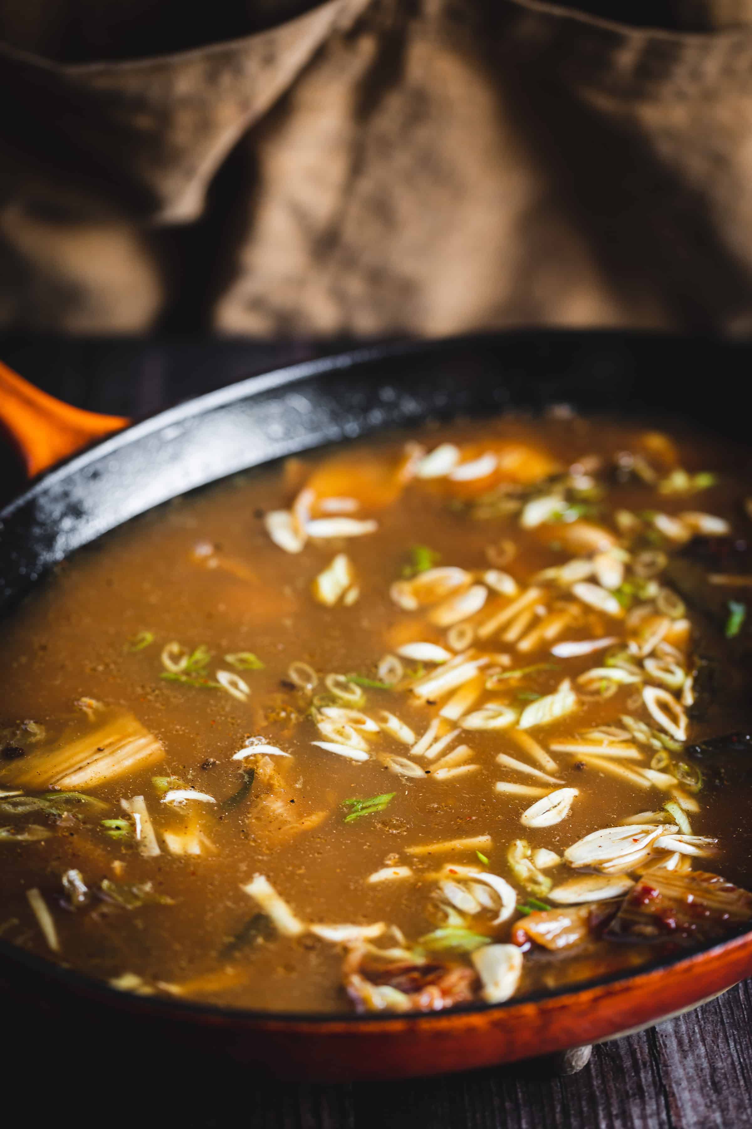 A close-up of a pot of soup with chopped green onions floating on the surface.