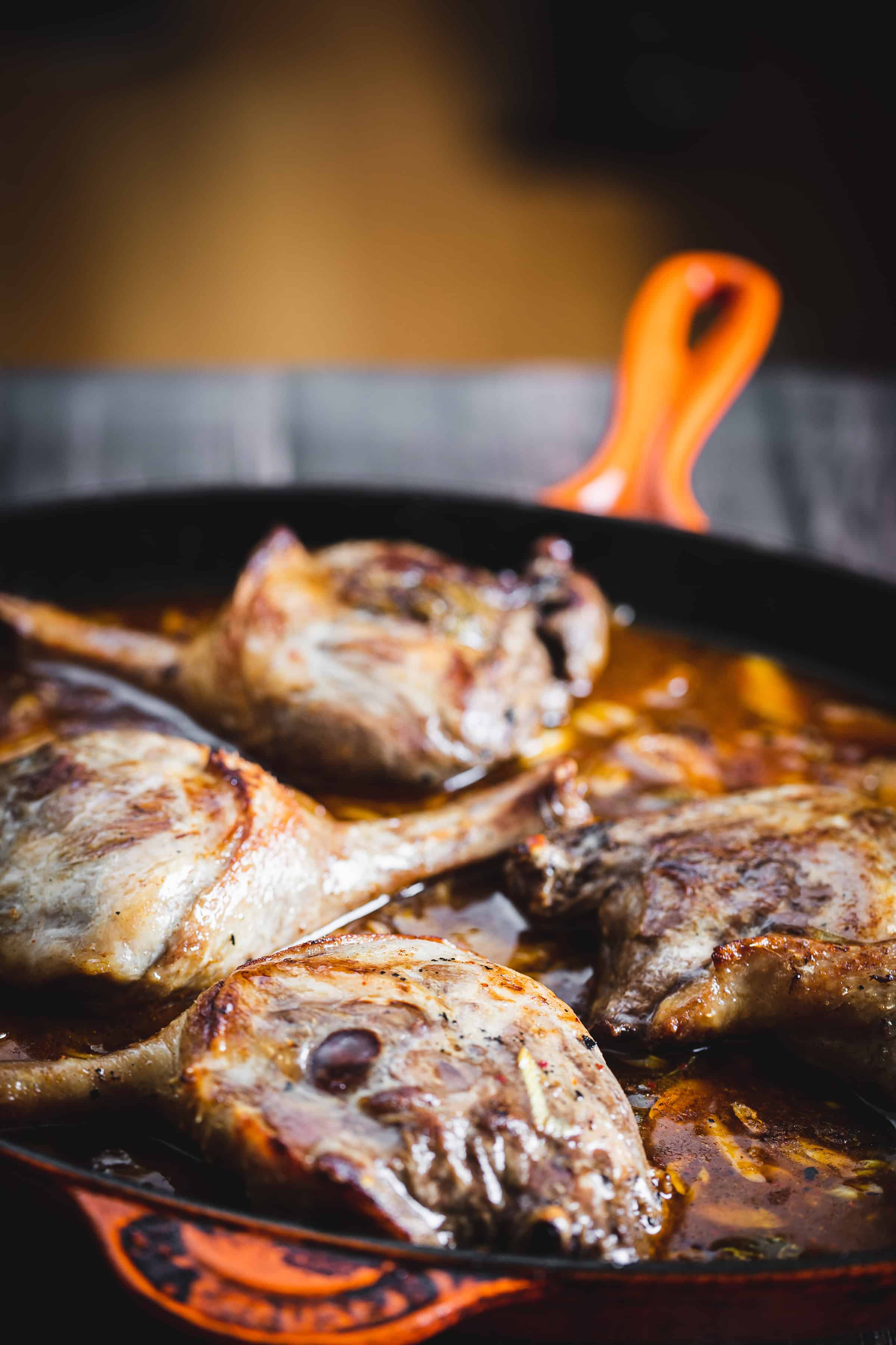 Four pieces of cooked meat simmering in sauce in an orange-handled cast iron skillet.