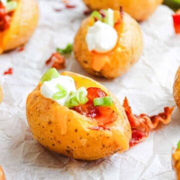 Mini baked potatoes topped with sour cream, bacon bits, cheddar cheese, and chopped green onions.