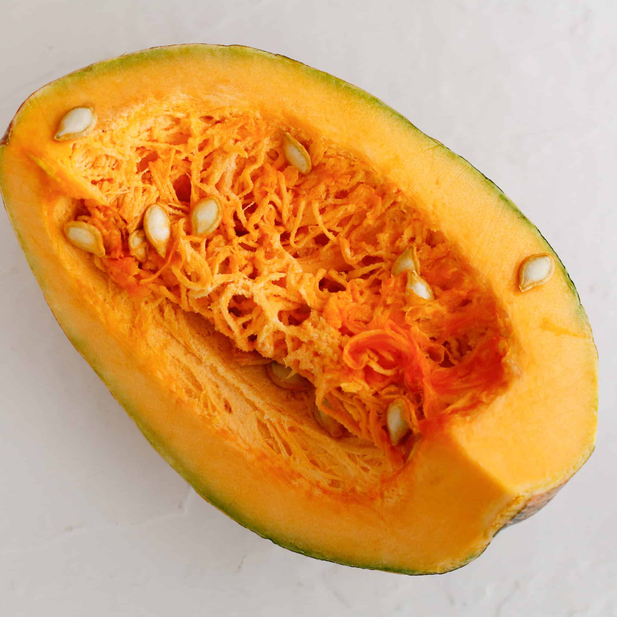 A close-up of a halved pumpkin showing its orange flesh and seeds on a white surface, perfect for making fresh pumpkin puree.