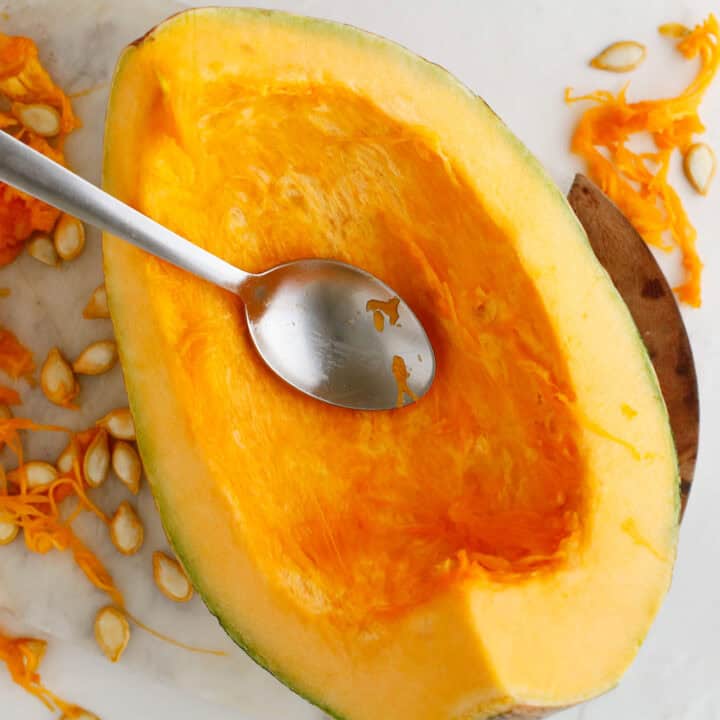 A metal spoon rests inside a half-scooped squash, with seeds and orange pulp scattered nearby&mdash;ready to be transformed into smooth pumpkin puree.